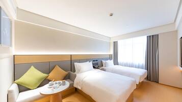 Hotellihuone, jossa on kaksi sänkyä, sohva, pieni pöytä ja ikkuna, jossa on verhot.