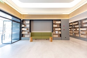 A modern library interior with a green bench, bookshelves, and a glass door entrance.