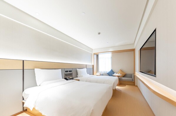 A hotel room with two beds, a TV, a desk, and a window.