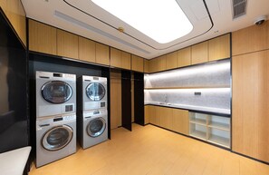 A laundry room with two front-loading washers and dryers, wooden cabinets, and a stainless steel sink.