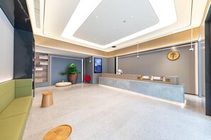 Ein moderner Empfangsbereich mit digitalem Bildschirm, einer Rezeption und einer Sitzecke mit einem grünen Sofa und Holzschemeln.