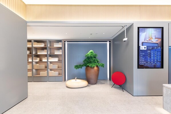 A modern lobby with a large digital display, a potted tree, and a red chair.