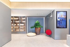 Moderni aula, jossa on suuri digitaalinen näyttö, ruukussa oleva puu ja punainen tuoli.