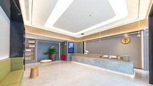 A modern reception area with a digital display, a reception desk, and a seating area with a green couch and wooden stools.
