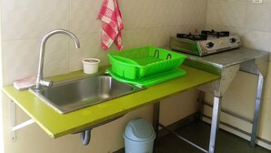 Een keuken met een spoelbak, een groen afdruiprek, een rood-witte handdoek en een bord met een blusapparaat op de muur.