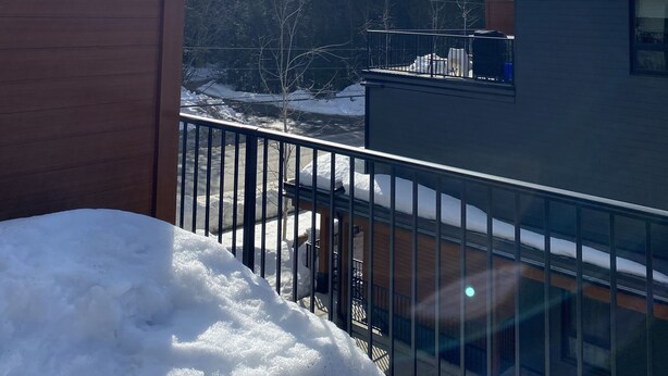En snötäckt balkong med fri utsikt över ett bergskedja och en träbyggnad i förgrunden.