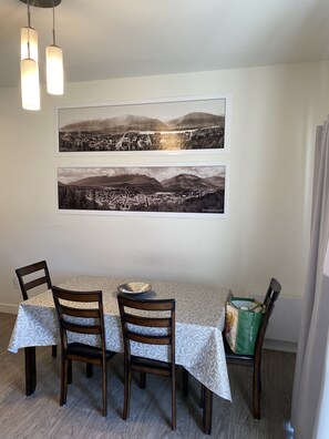 Un coin repas avec une table dressée pour deux personnes, deux chaises et une grande photographie encadrée accrochée au mur.