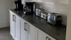 Ett modernt kök med vita skåp, en svart bänkskiva och rostfria köksapparater, inklusive en kaffebryggare, brödrost och förvaringsburkar.