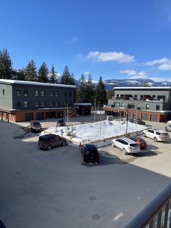 A parking lot with several cars, a building with multiple windows, and a snowy mountain backdrop. - Cozy Condo minutes from RMR & Soon Cabot Pacific Golf (Revelstoke)