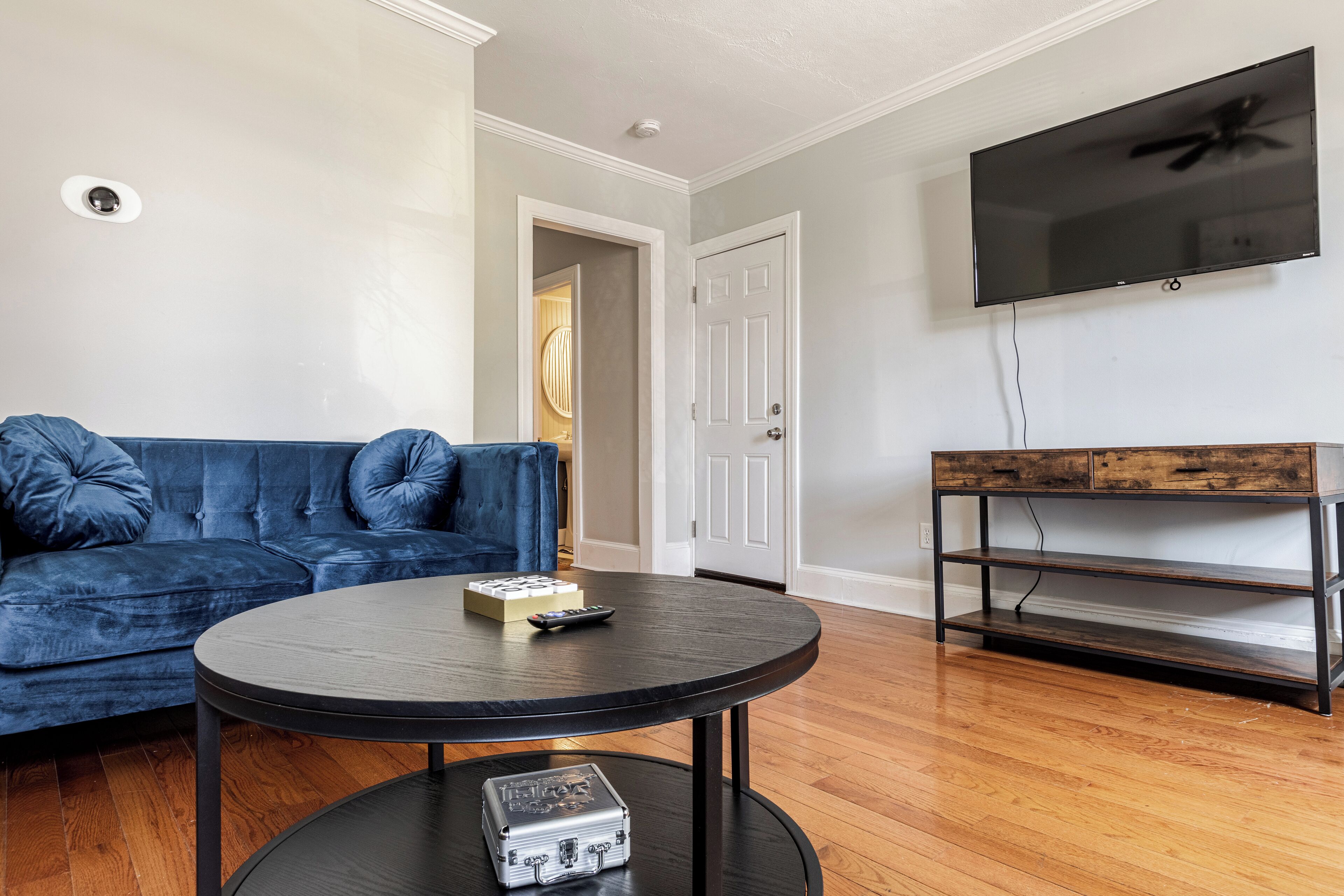 Un salon avec un canapé bleu, une table basse ronde, un meuble TV en bois et un téléviseur à écran plat fixé au mur.