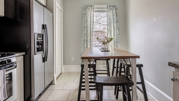 Een keuken met een zwarte koelkast, witte kasten, een houten tafel en een raam met gordijnen met een patroon.
