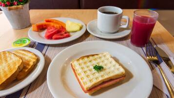 A breakfast setting with toast, a sandwich, fruit, a cup of coffee, and a glass of juice on a table.