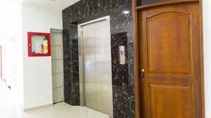 Um hall de hotel com parede de mármore, um elevador e uma porta de madeira.