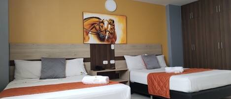 A hotel room with two beds, a wooden headboard, a painting of horses, a wardrobe, and a nightstand with a lamp.