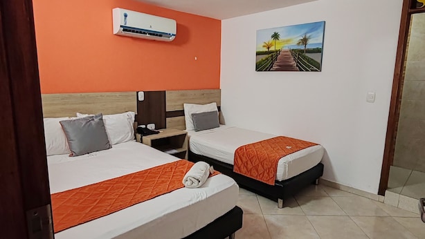 Quarto de hotel com duas camas, ar condicionado, mesa de cabeceira, um quadro e piso em azulejo.