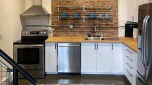 A modern kitchen with a brick wall, stainless steel appliances, and a wooden countertop.