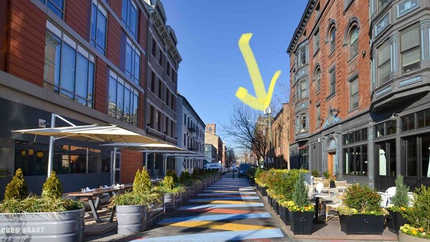 A street with colorful pedestrian crossings, outdoor seating, and buildings with large windows.