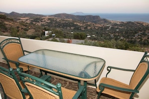 Um terraço com mesa de vidro e cadeiras de vime, com vista para uma paisagem montanhosa.
