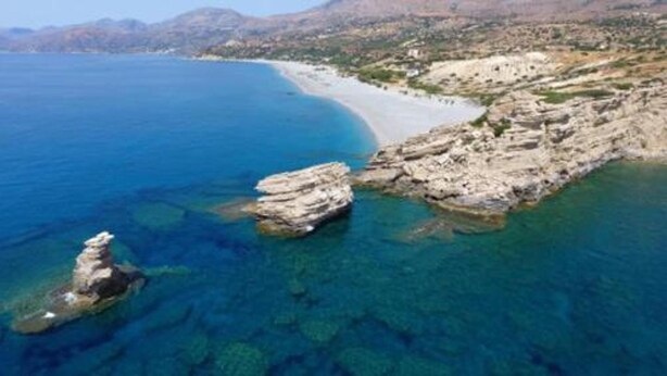 A coastal landscape with clear blue waters, rocky outcrops, and a sandy beach. - Paterakis Big Studio in Triopetra (Agios Vasileios)