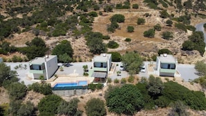 Vista aérea de um bairro residencial com três casas modernas, uma piscina e vegetação ao redor.