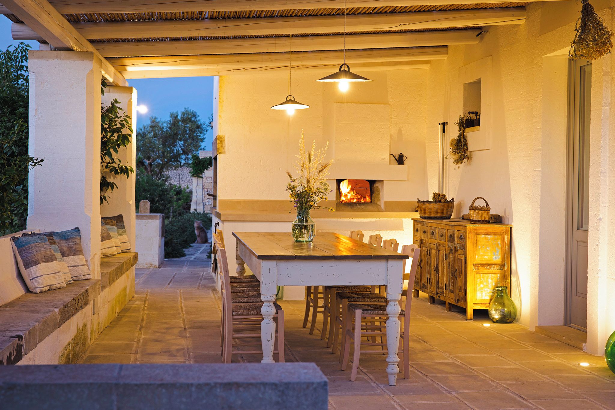 An outdoor dining area with a table and chairs, a fireplace, and a stone bench.