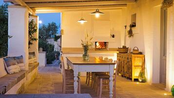 Un espace extérieur aménagé pour les repas, avec une table et des chaises, une cheminée et un banc en pierre.