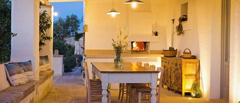 An outdoor dining area with a table and chairs, a fireplace, and a stone bench.