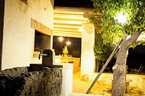 An outdoor dining area with a stone fountain, a wooden table, and chairs. - Masseria Ferarelli Trepizzi (Diso)