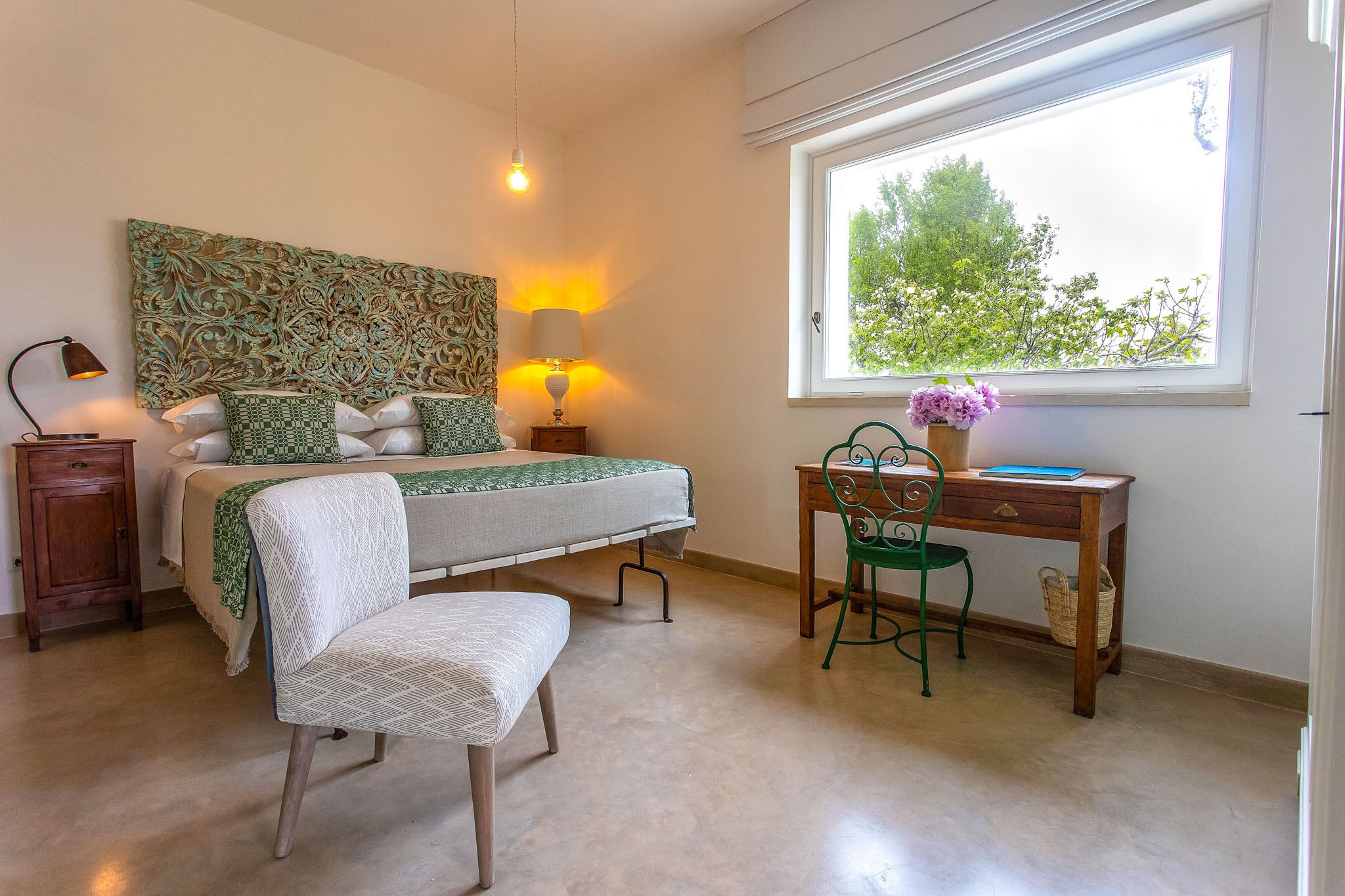 Une chambre à coucher comprenant un lit, des lampes de chevet, un bureau, une chaise et une fenêtre donnant sur des arbres.