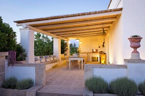 An outdoor patio area with a covered seating area, a table, and a fireplace. - Masseria Ferarelli Trepizzi (Diso)