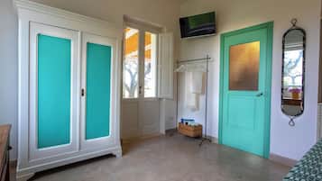 A room with a teal door, a white wardrobe, a TV mounted on the wall, and a mirror.