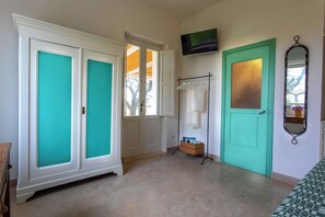 A room with a teal door, a white wardrobe, a TV mounted on the wall, and a mirror. - Masseria Ferarelli Trepizzi (Diso)