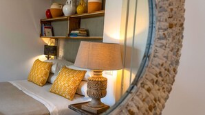 A bedroom with a bed, a bedside table with a lamp, and a shelf with books and decorative items. - Masseria Ferarelli Trepizzi (Diso)