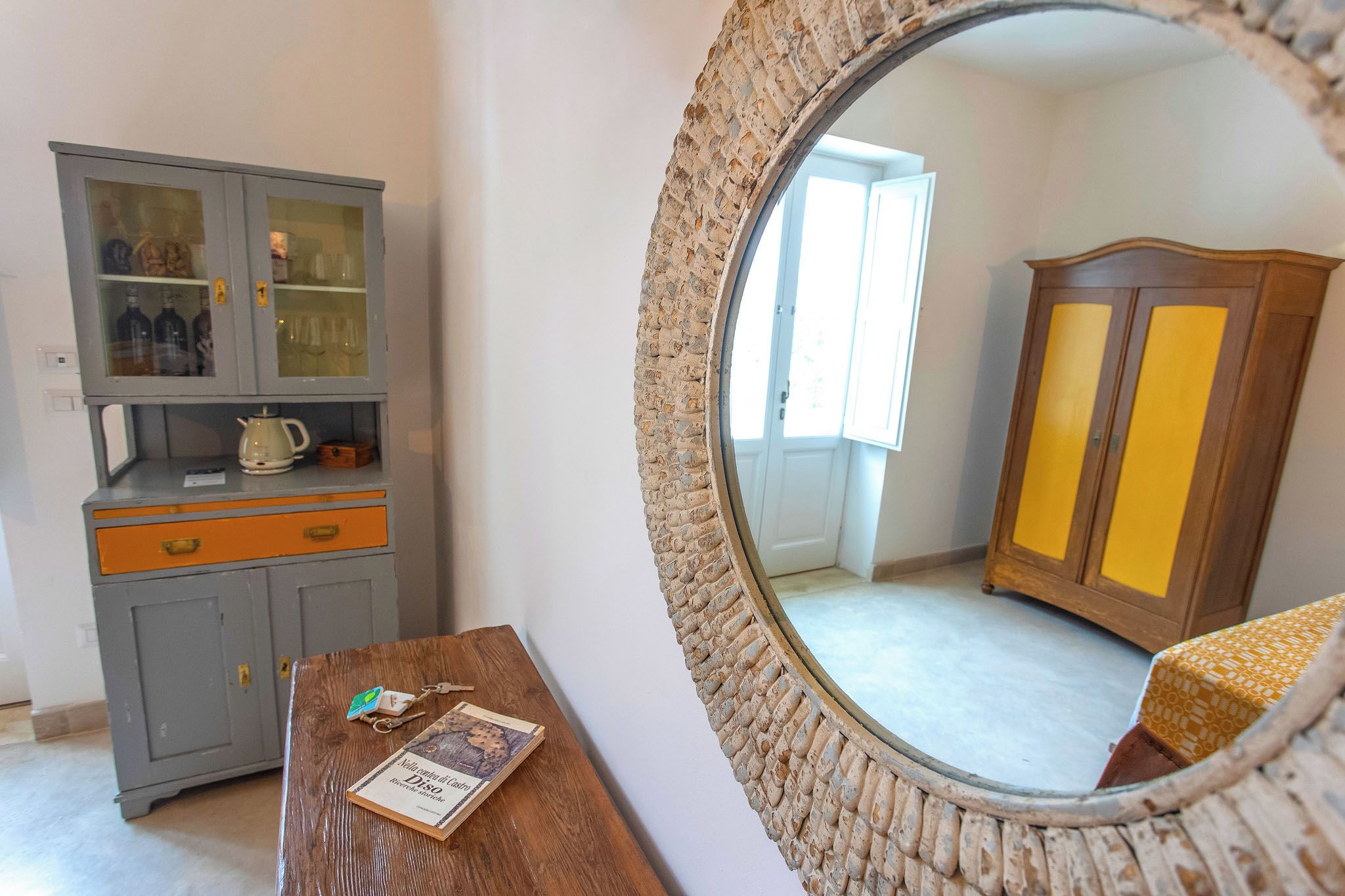 A room with a wooden cabinet, a small table with a book, and a mirror with a brick frame.