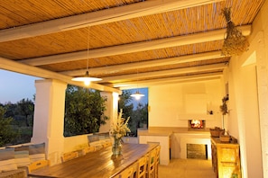 An outdoor dining area with a wooden table and chairs, a hanging light fixture, and a fireplace. - Masseria Ferarelli Trepizzi (Diso)