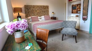 A bedroom with a bed, bedside lamps, a chair, a table with a vase of flowers, and a dresser with decorative items.