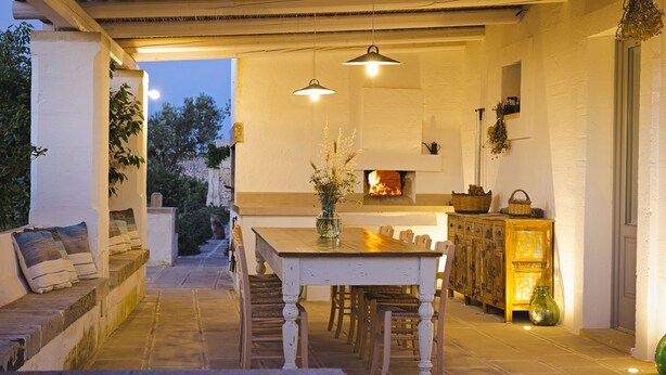A cozy outdoor dining area with a table and chairs, a fireplace, and hanging lights. - Masseria Ferarelli Trepizzi (Diso)