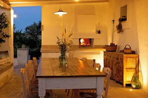 An outdoor dining area with a wooden table and chairs, a vase with flowers, and a fireplace in the background. - Masseria Ferarelli Trepizzi (Diso)