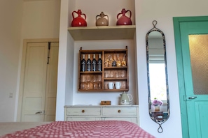 A bedroom with a bed, a dresser, a shelf with bottles and glasses, a mirror, and a door. - Masseria Ferarelli Trepizzi (Diso)
