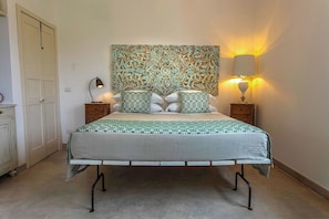 A neatly arranged bedroom with a bed, two bedside tables, a decorative wall hanging, and a wall-mounted lamp. - Masseria Ferarelli Trepizzi (Diso)