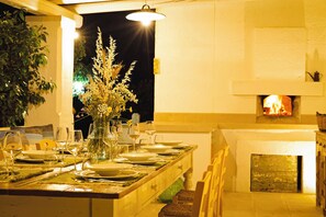 A dining area with a table set for four, a vase of flowers, and a fireplace in the background. - Masseria Ferarelli Trepizzi (Diso)