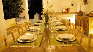 A dining table set for a meal with chairs, a vase with flowers, and a fireplace in the background.