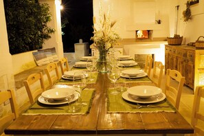 A dining table set for a meal with chairs, a vase with flowers, and a fireplace in the background.