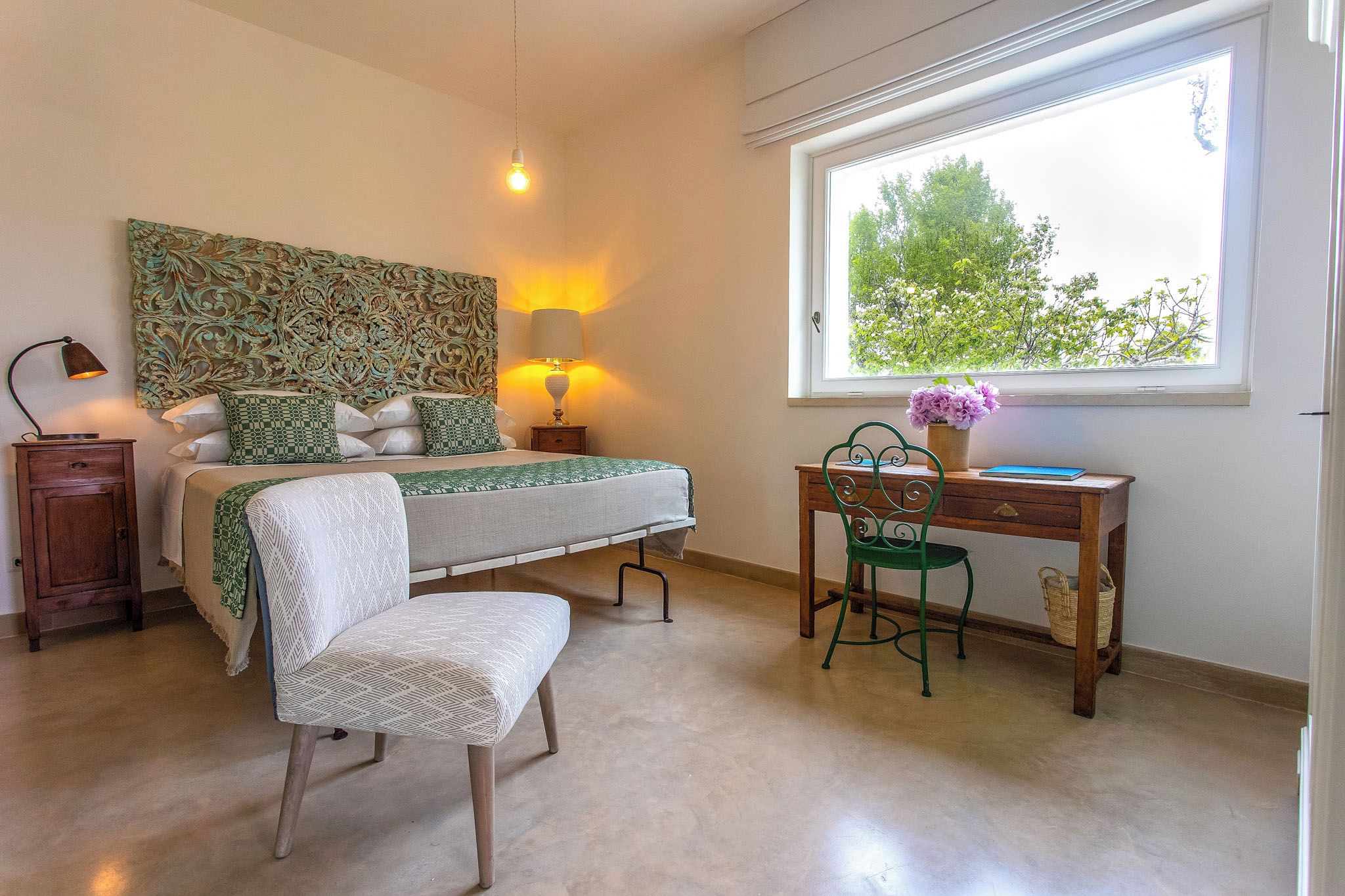 Une chambre à coucher comprenant un lit, des lampes de chevet, un bureau, une chaise et une fenêtre donnant sur des arbres.
