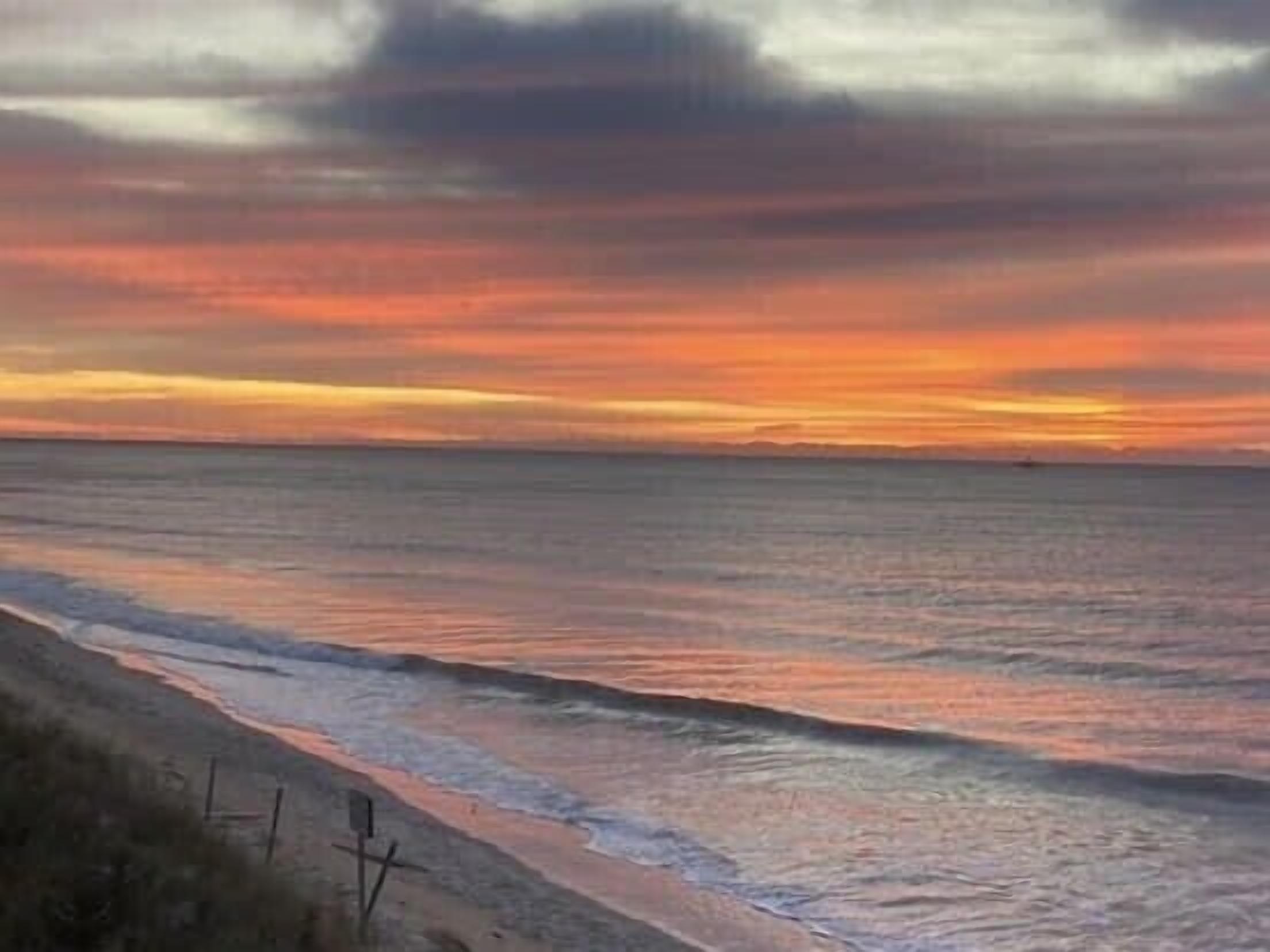 A beach with a sunset, calm sea, and a sandy shore.