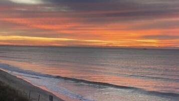 A beach with a sunset, calm sea, and a sandy shore.
