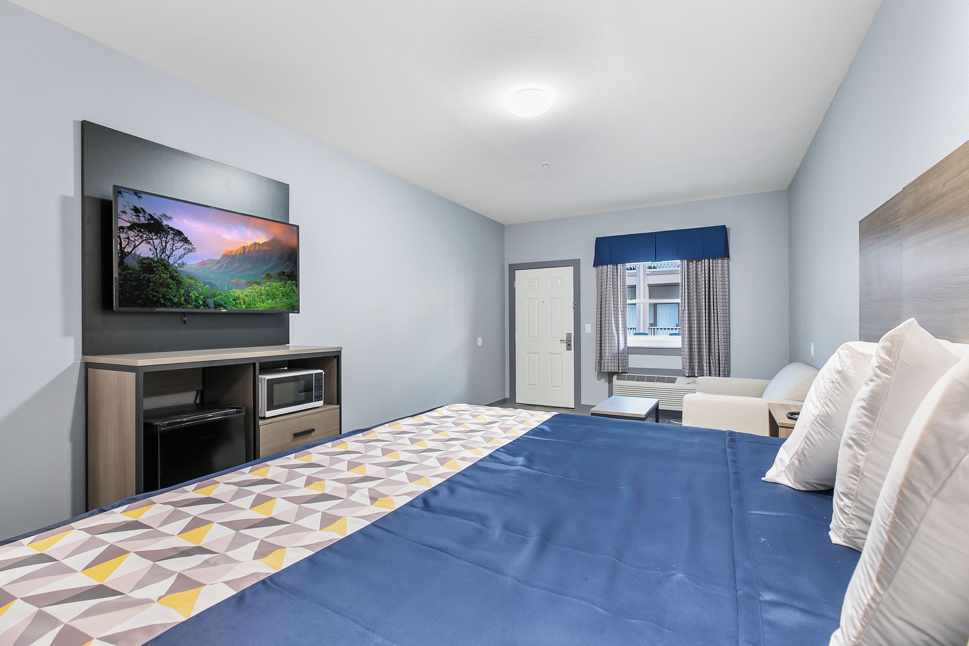 Ett modernt hotellrum med en stor säng, en platt-TV, ett skrivbord och en sittgrupp.