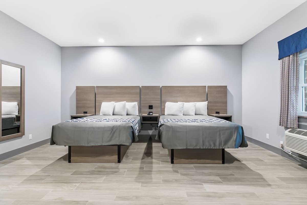 Una habitación de hotel moderna con dos camas individuales, un espejo grande, una mesita de noche pequeña y un equipo de aire acondicionado integrado.