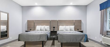 A modern hotel room with two single beds, a large mirror, a small bedside table, and a built-in air conditioning unit.
