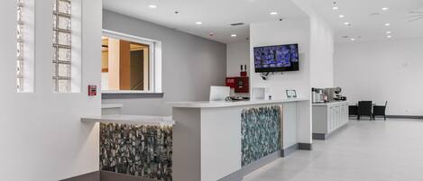 A modern reception area with a counter, a television mounted on the wall, and a seating area with chairs.